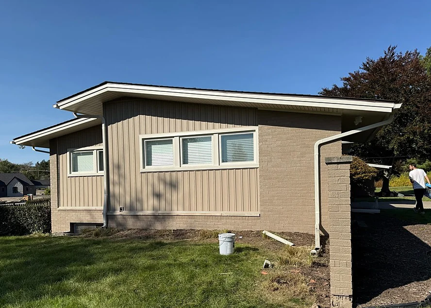 The same ranch wall with brick and siding painted in matching taupe and white window trim
