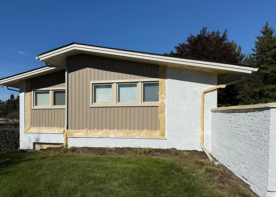 The same ranch wall with white-primed brick and paper masking along window and siding edges