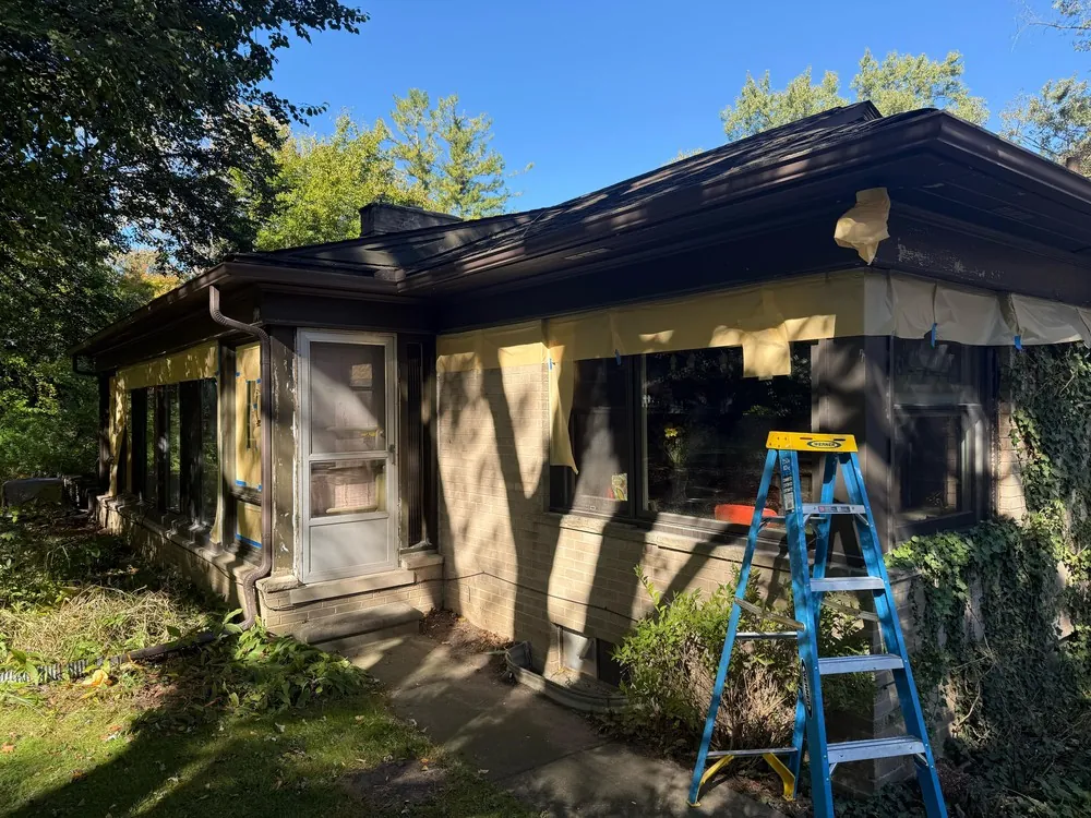Paper masks brick above windows beside a ladder on a ranch exterior