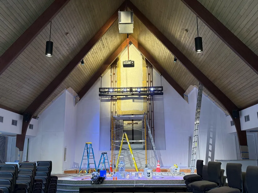 Church sanctuary with a vaulted wood ceiling, masked windows and access equipment during painting