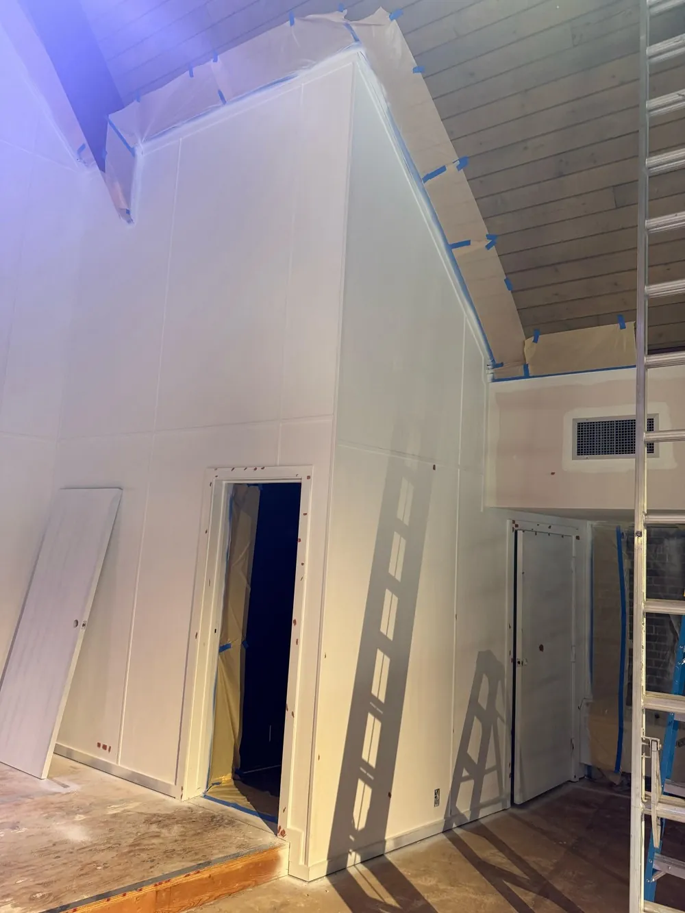 Paper and blue tape protecting a wood ceiling edge above white church walls