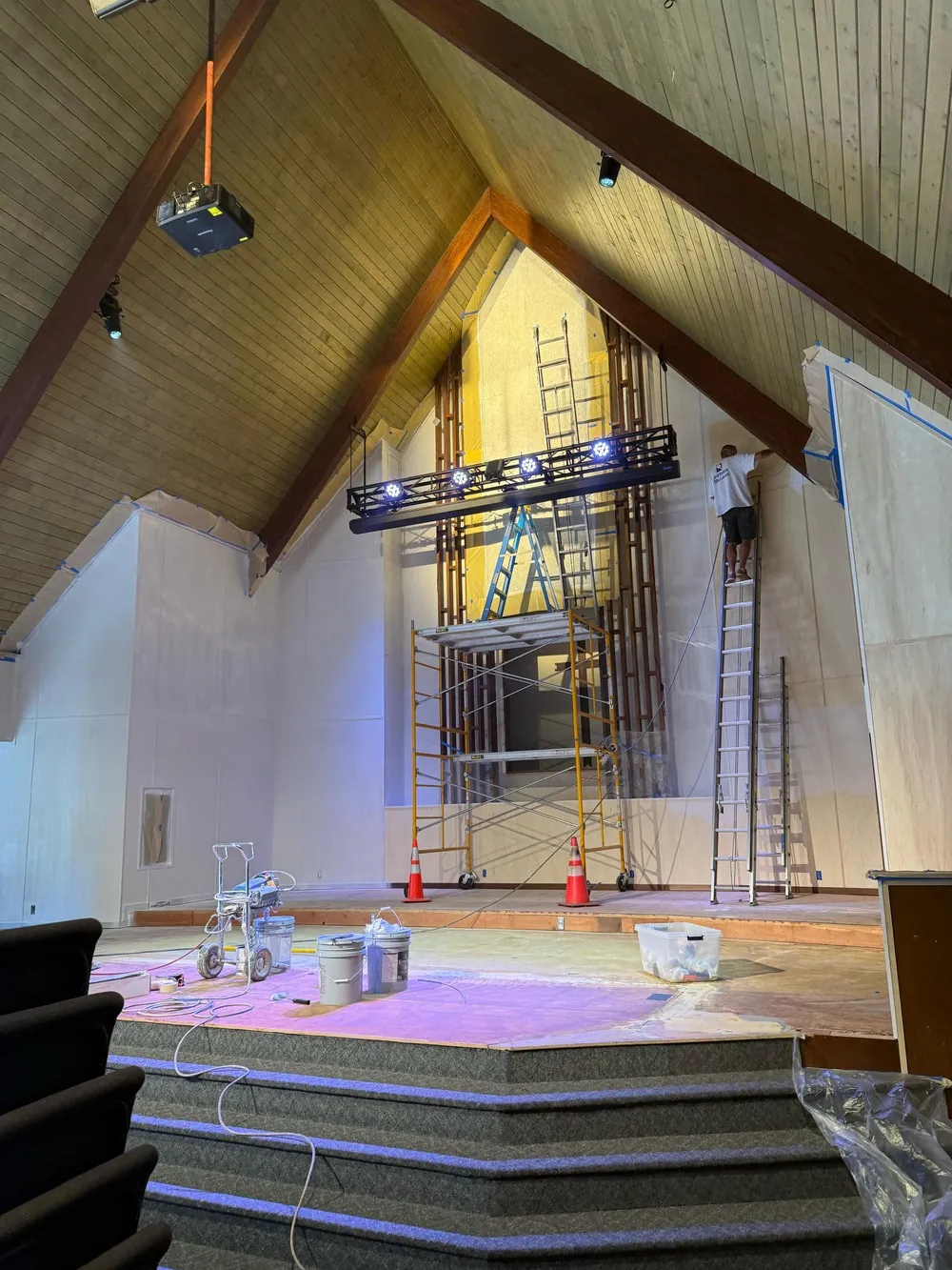 Worker on a ladder beside tall sanctuary walls with scaffolding and masked windows