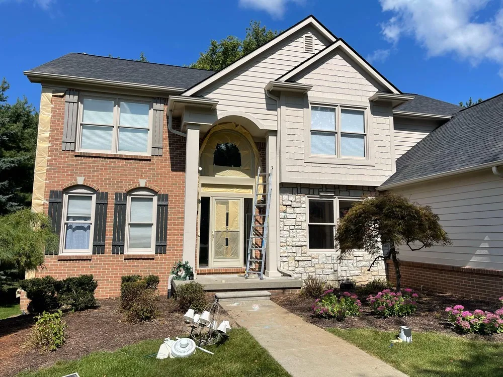 Brick and cream-sided colonial with a masked entry and ladder during exterior painting