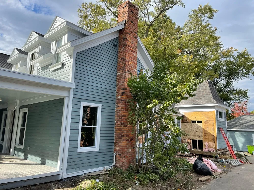 Farmhouse corner with scraped siding next to a brick chimney