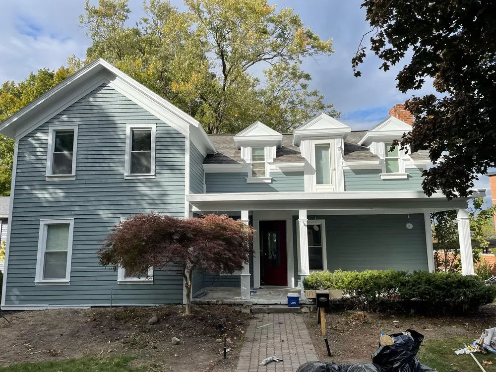 Painted gray-green farmhouse siding and white trim with work materials still outside
