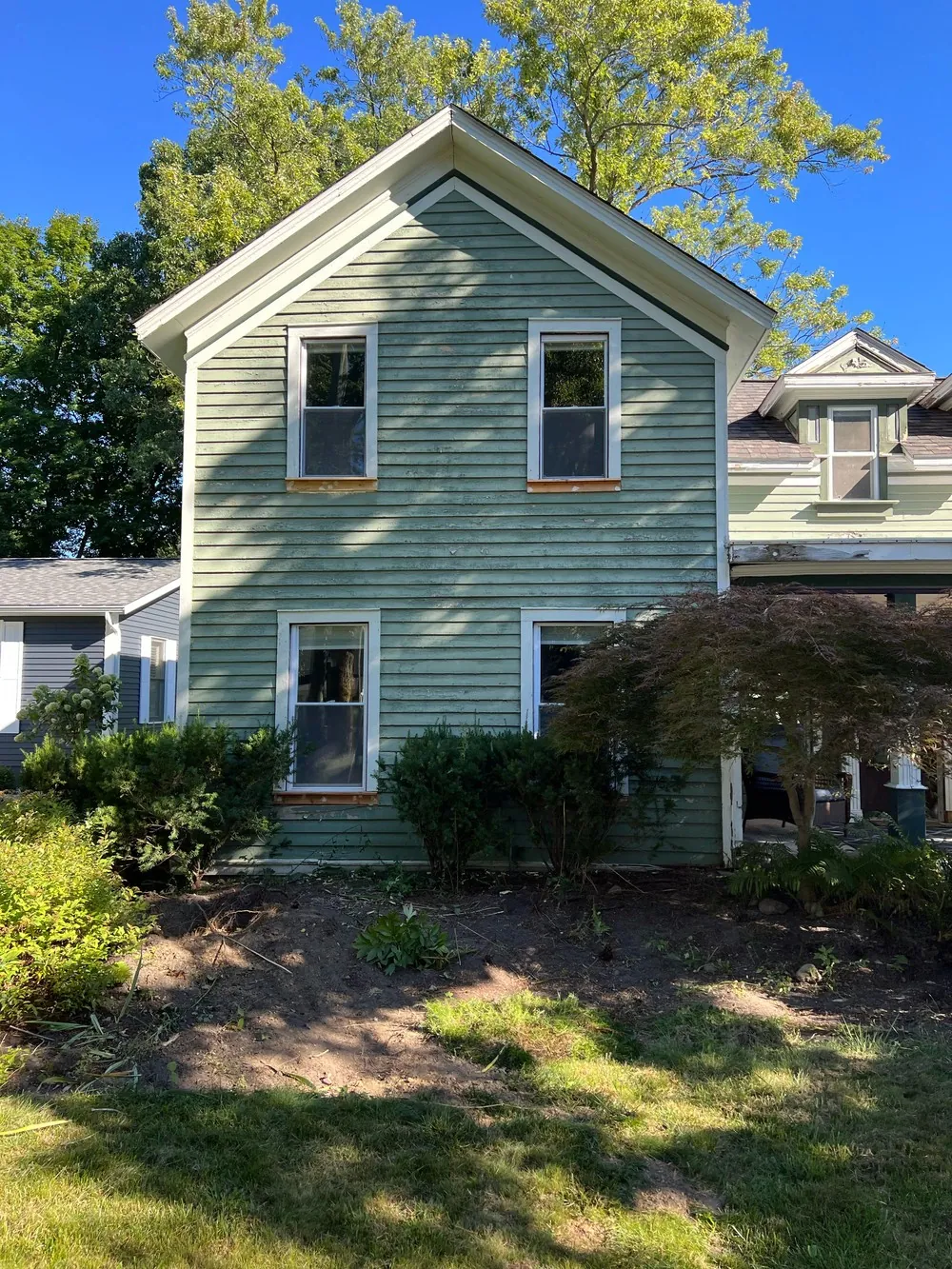 Gable end of a sage-green farmhouse with white window trim