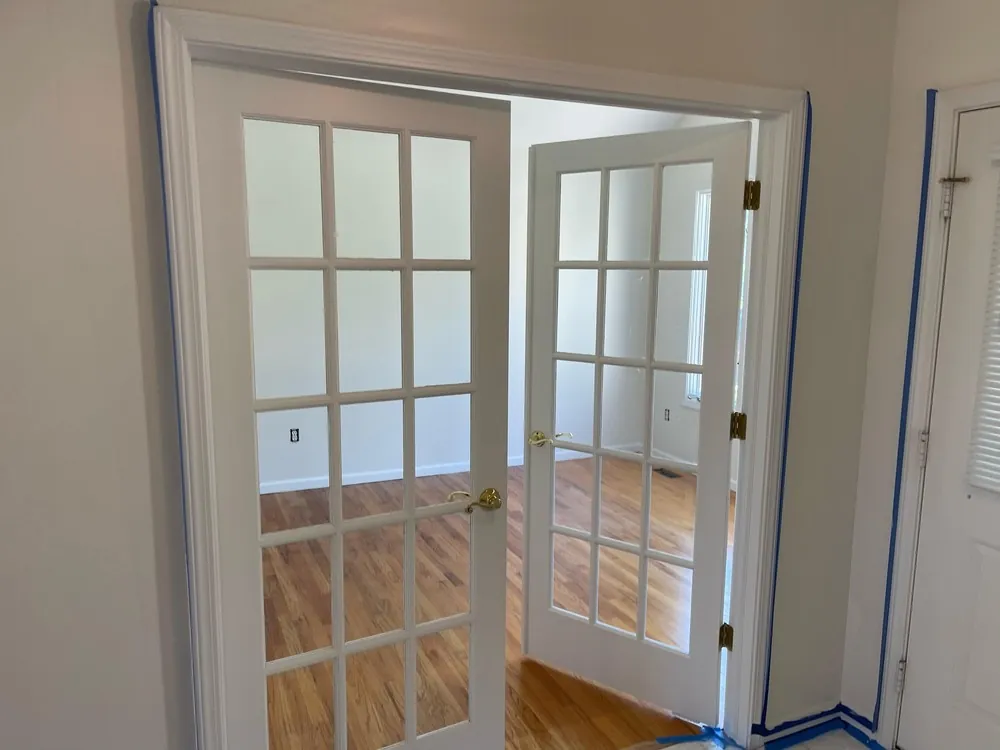 White French doors opening onto a wood-floored room, with masking tape still around the trim