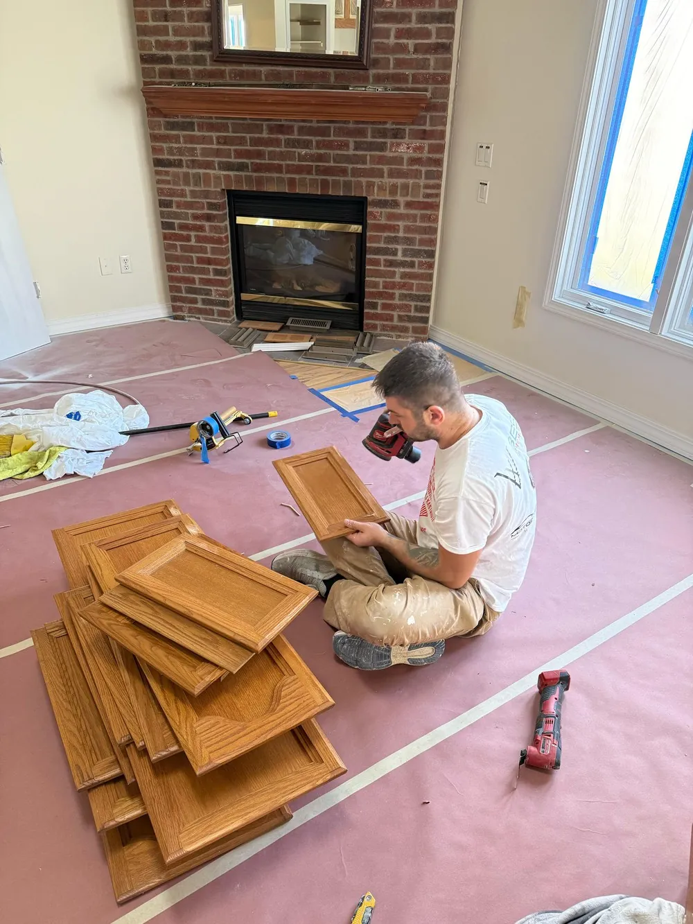 Painter sanding kitchen cabinet doors laid out on protective paper