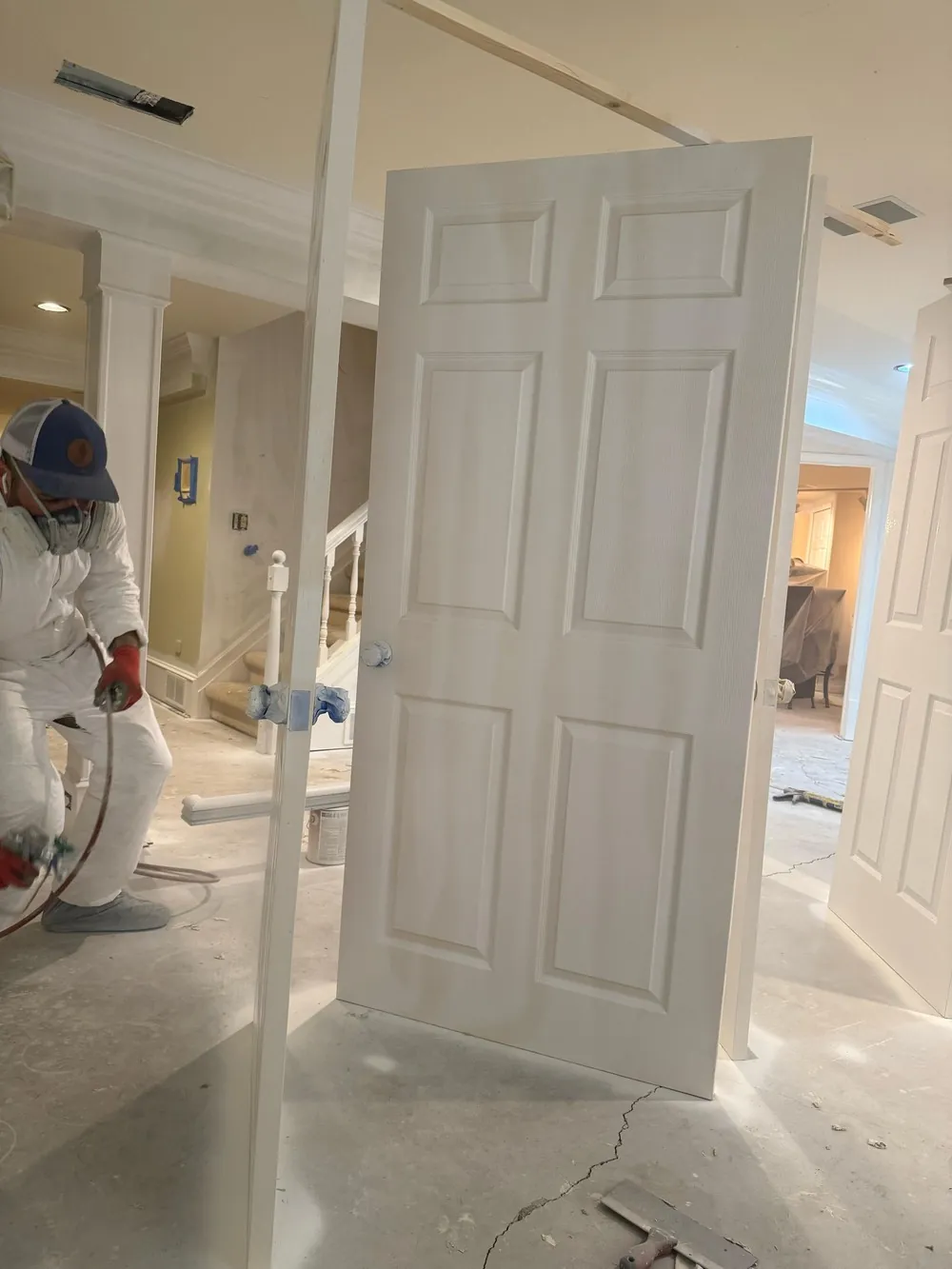 Painter in a protective suit working with a spray gun beside removed interior doors