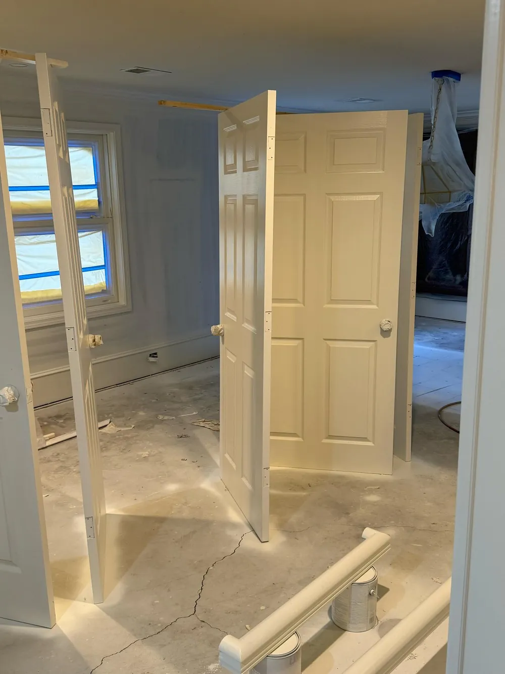 Removed white interior doors standing in a work area with masked windows and a covered light fixture