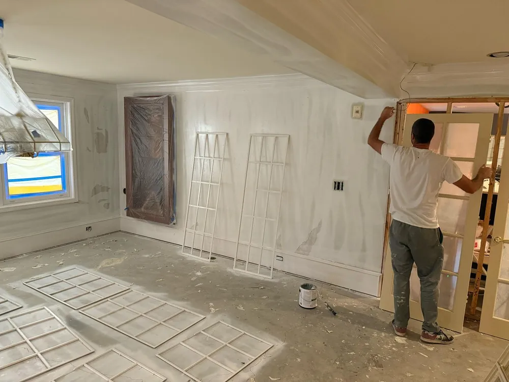 Painter fitting trim in a living room with white paneling