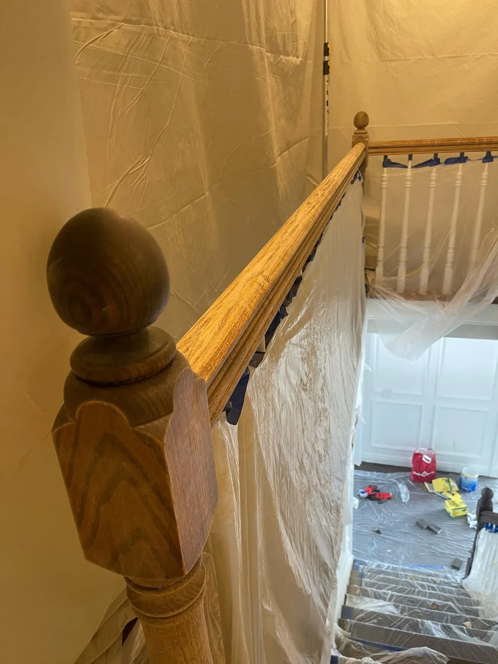 Stair treads and balusters covered with plastic while a wood handrail is prepared