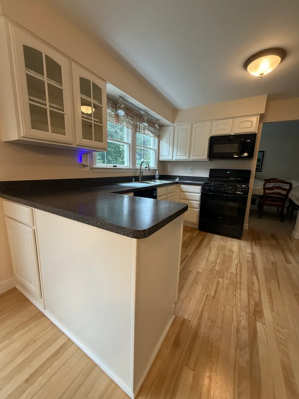 White cabinet doors and a dark peninsula countertop beside a window and black range
