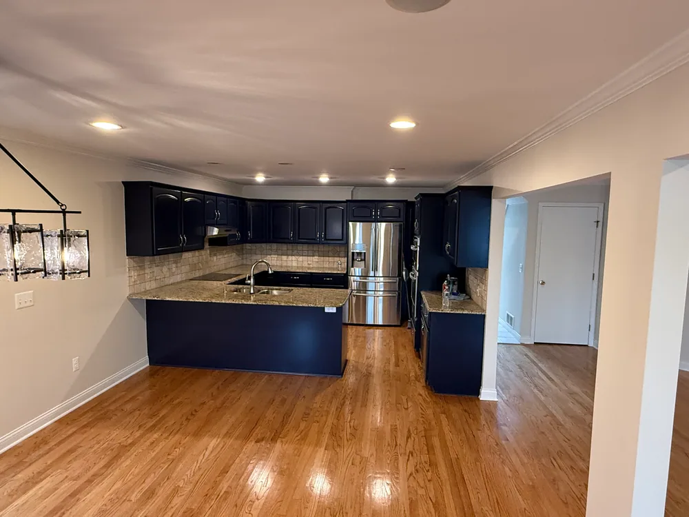 Dark blue kitchen cabinets with a stainless refrigerator and a light wood floor