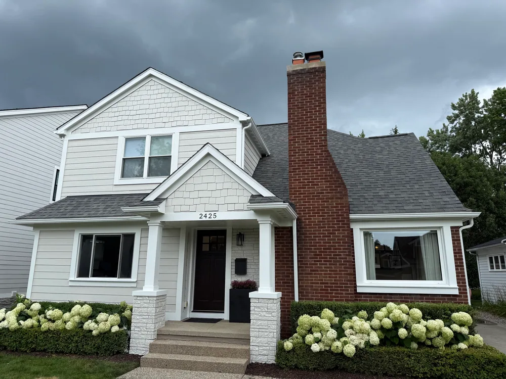 Gabled house with light-gray siding, white trim, a brick chimney and hydrangeas