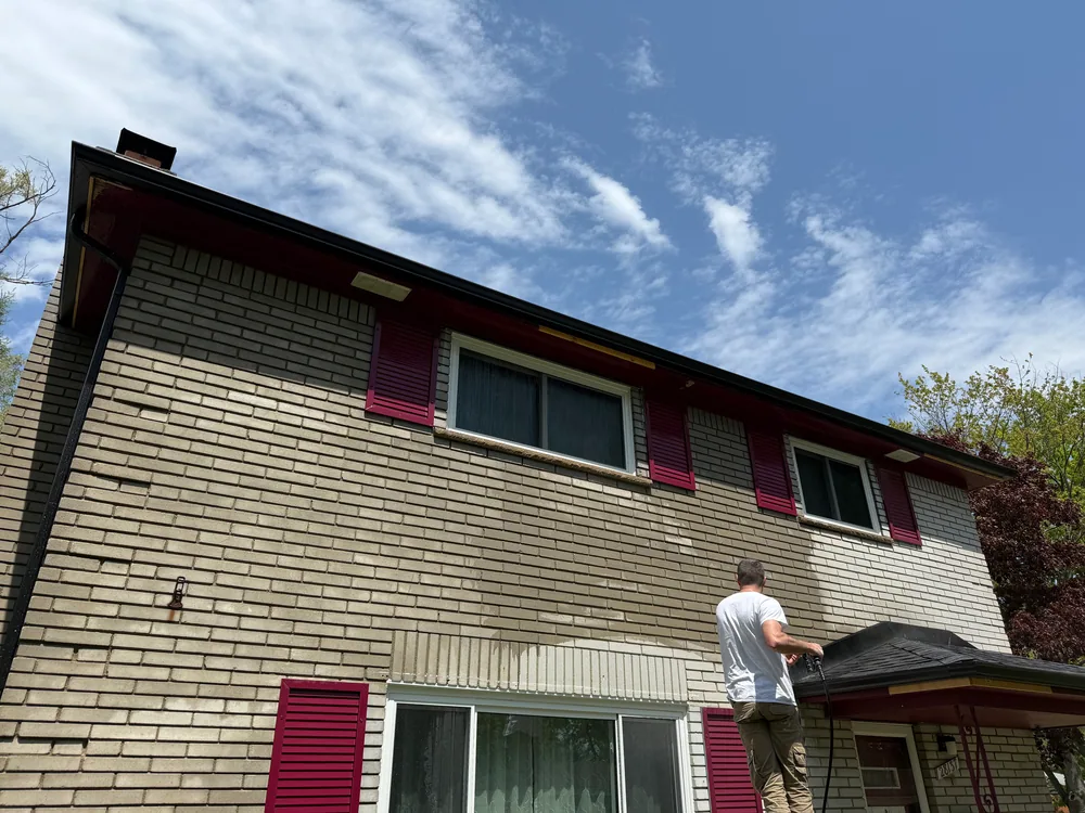Worker holding a washing wand in front of a light brick house with red shutters