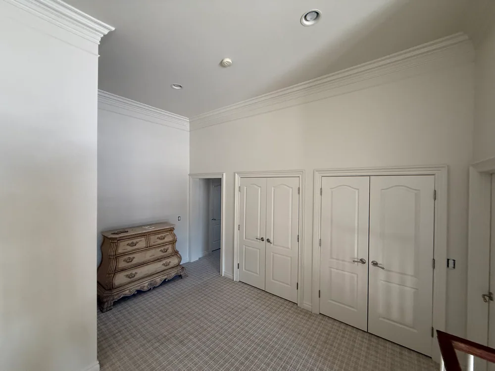 Light-colored upstairs walls above two white closet-door pairs and a wood dresser