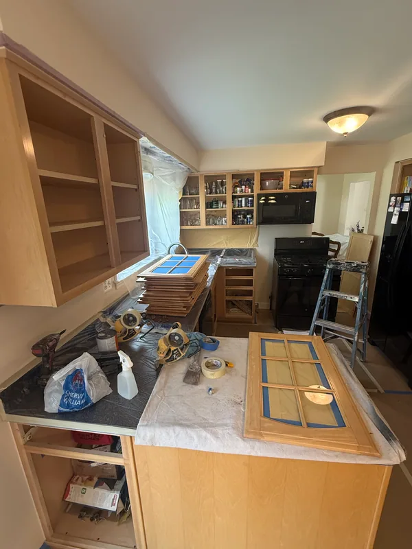 Removed glass cabinet doors with masked panes beside open wood cabinet boxes.
