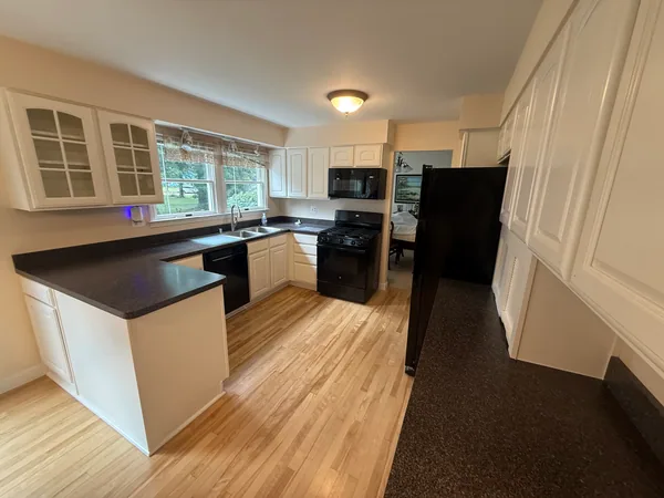 White kitchen cabinets with black appliances, dark countertops and a light wood floor
