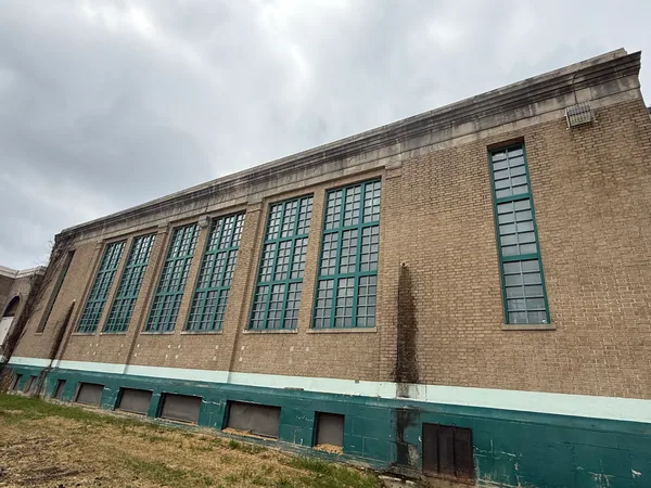 Beige brick facade with tall green window frames and weathered green lower walls.