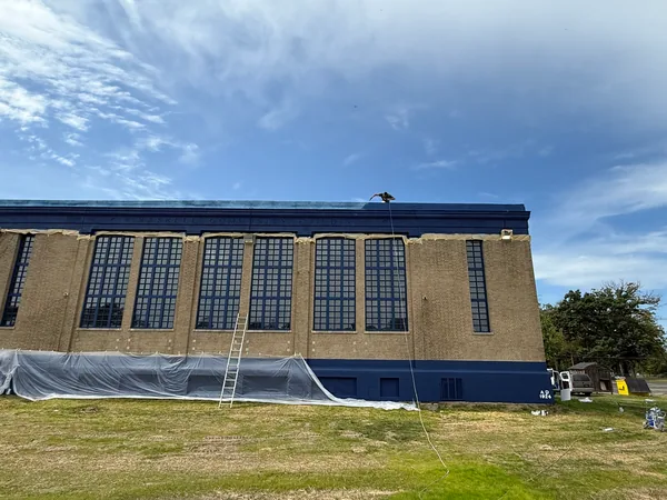 Blue-accented brick facade with a ladder and plastic sheeting along the base.