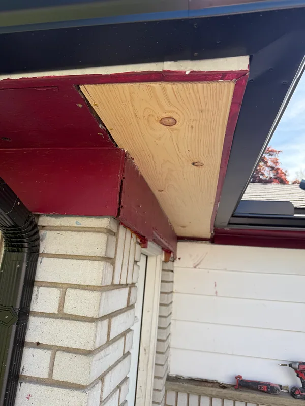 Exposed wood soffit section beside red painted trim and a black gutter
