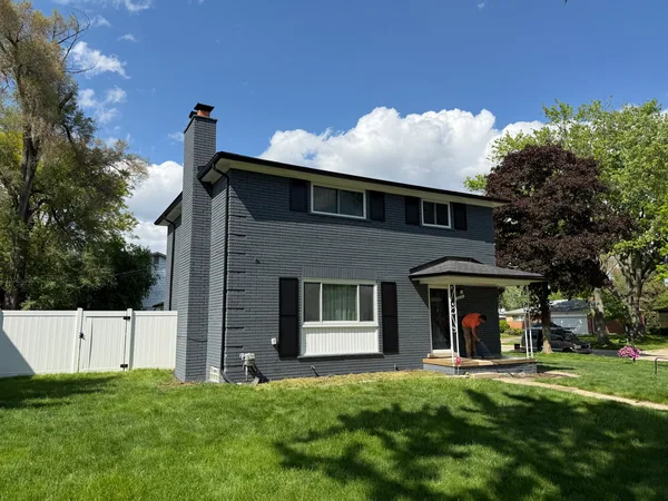 Dark gray brick house with black shutters and white trim, with a worker at the porch