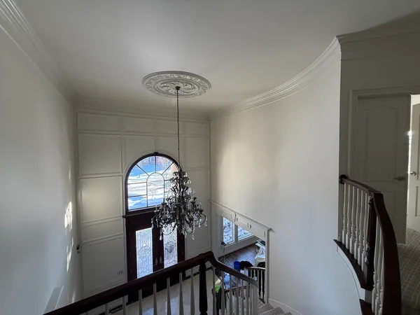 Light-colored entryway walls beside an arched window, white paneling and a curved stair rail