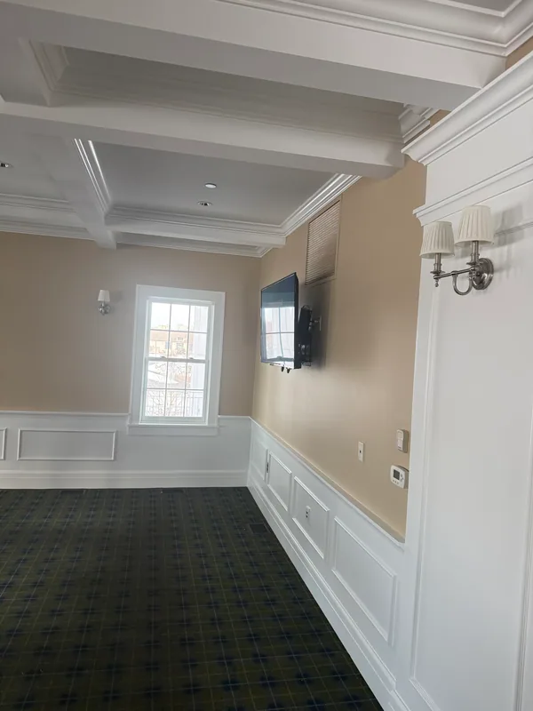 Light lounge walls with white panels, molding and a coffered ceiling above a patterned carpet