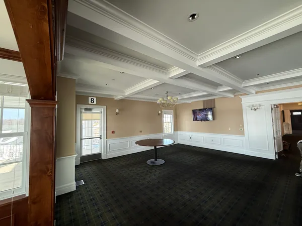 Cleared lounge with light walls, white paneling, a coffered ceiling and a round table